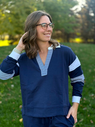 Navy long-sleeve pullover with striped neckline trim, contrasting sleeve panels, and side-slit hem.