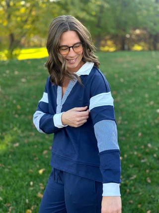 Angled view of navy collared pullover showing white sleeve bands, striped panels, and white cuffs.