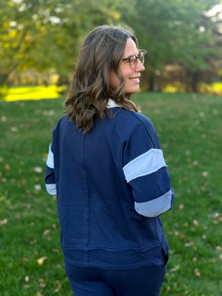 Back view of navy pullover with white sleeve bands, striped elbow panels, and a center back seam.