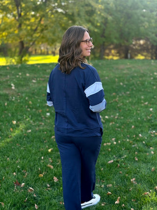 Full-length back view of navy matching set with white sleeve bands, striped elbow panels, and wide-leg pants.

