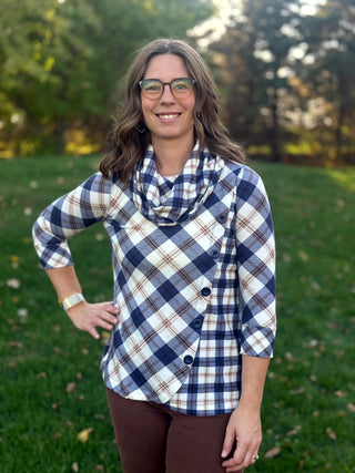  Model posing with one hand on her hip in a navy and cream plaid cowl-neck top with diagonal buttons and an asymmetrical hem.