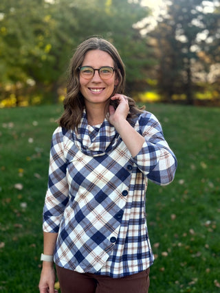 Model wearing a navy and cream plaid cowl-neck top with three-quarter sleeves and diagonal buttons, one hand near the neckline.