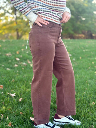 Angled view of brown wide-leg jeans with rolled hems, styled with white and black sneakers.