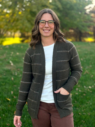 Close-up front view of a dark olive striped cardigan with ribbed trim and a hand resting in a patch pocket.
