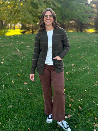 Full-length front view of a model wearing a dark olive striped cardigan over a white top with brown pants.