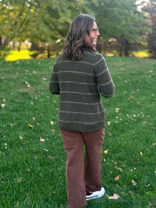 Model wearing a dark olive cardigan with thin cream horizontal stripes, shown from the back with brown pants.