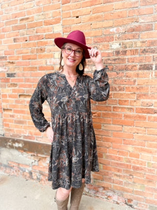 Woman wearing a floral dress and red hat against a brick wall