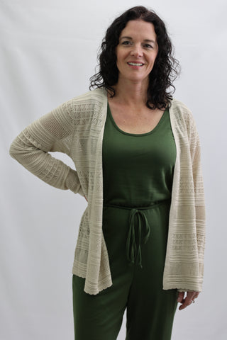 Woman wearing a beige cardigan over a green top and pants on a white background