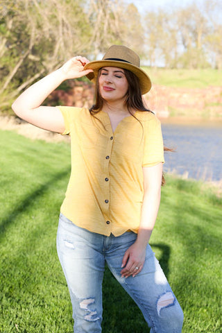 Woman wearing a yellow shirt and hat in a grassy outdoor setting