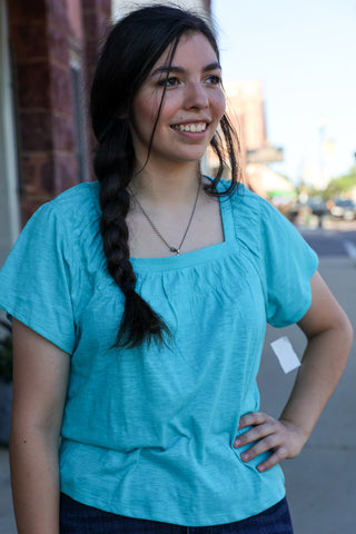 Woman wearing a blue shirt standing outdoors with a blurred background